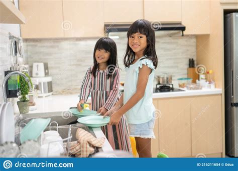 Happy Young Girl Are Doing Dish Washing Together In The Kitchen Sink