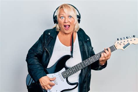 Middle Age Blonde Woman Playing Electric Guitar Using Headphones Afraid