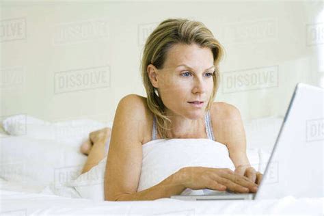 Woman Lying On Bed Using Laptop Computer Looking Away Stock Photo Dissolve