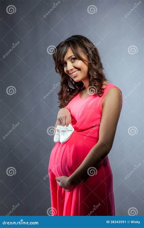 Жизнерадостная беременная женщина представляя с добычами младенца
