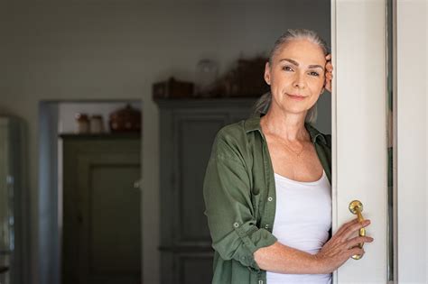 Portrait Of Senior Woman Leaning Against Door At Home And Lookin