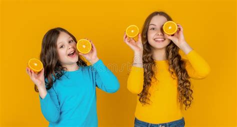 Smiling Teen Girls Hold Orange Fruit On Yellow Background Stock Image