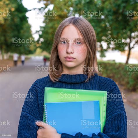 teenage girl of 1315 years old on autumn day stands on street in city holds notebooks with
