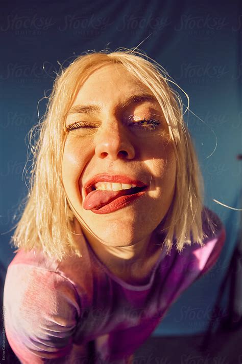funny portrait of a blond woman winking an eye and showing her tongue by stocksy contributor