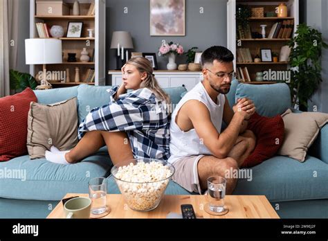 Stressed Young Married Couple Sitting Separately On Different Sides Of Sofa Ignoring Each Other