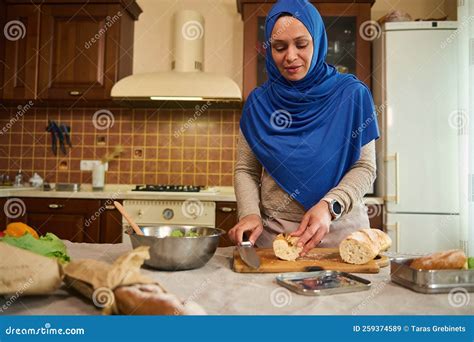 muslim arab housewife in hijab cutting loaf of whole grain bread and making sandwiches with