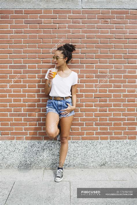 Young Woman Leaning Against A Brick Wall Drinking Orange Juice