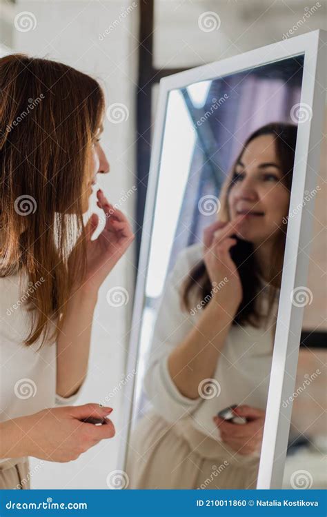 cheerful brunette woman applying lipstick balm on lips in front of mirror makeup beauty care