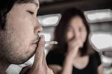 passive smoking concept asian man smoking cigarette and woman is covering her face stock