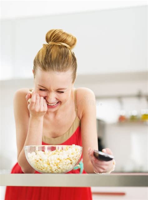 Laughing Young Woman Eating Popcorn And Watching Tv In Kitchen Stock