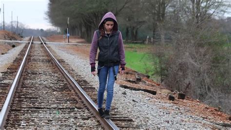 Sad Teen Girl With Earphones And Hoodie Standing On Train Tracks Stock