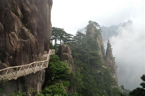 A Wooden Walkway Clings To The Side Of A Sheer Cliff Overlooking Peaks