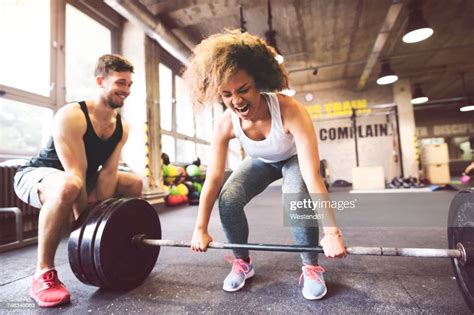Young Woman With Training Partner Preparing To Lift Barbell In Gym