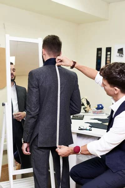 Portrait Of Young Tailor Measuring Back Of Handsome Man Fitting Bespoke
