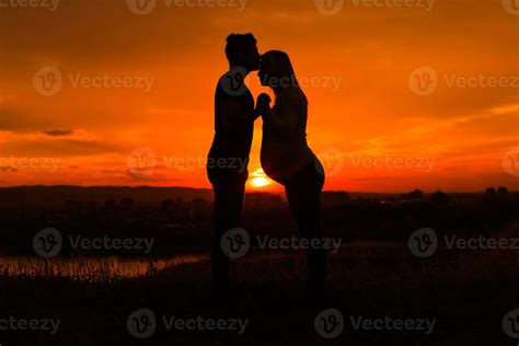 Silhouettes Of Husband Kissing His Pregnant Wife Into Forehead And
