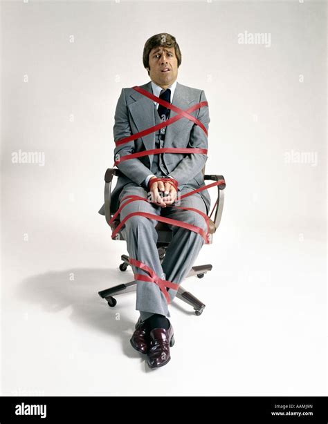 1970s Business Man Tied Up In Red Tape Sitting In Office Desk Chair