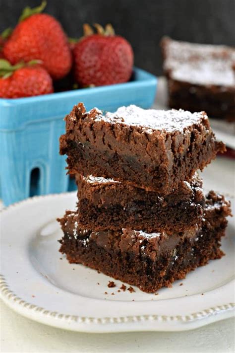 Three Chocolate Cake Bars Stacked Up On A White Plate With A Bowl Of