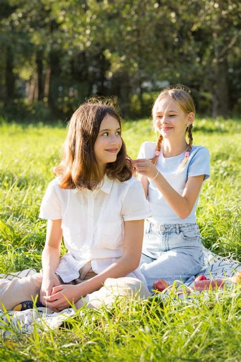 Two Teenage Girls Spend Time On Green Grass Lawn In Park Stock Photo