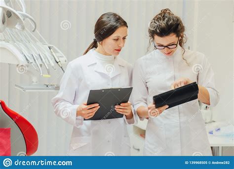 Portrait Of A Smiling Dentist And Assistant Looking At The Clipboard In A Modern Dental Clinic