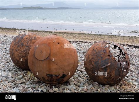 Three Old And Rusty Buoys Stranded On A Pebble Beach Near The Shoreline