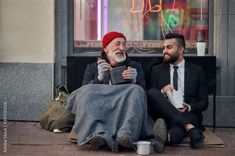 Handsome Businessman In Suit Sitting On Floor With Homeless Man Together Listen To His Story Of