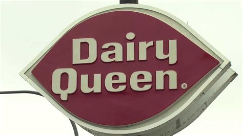 A Dairy Queen Sign Hanging Off The Side Of A Building In Front Of A