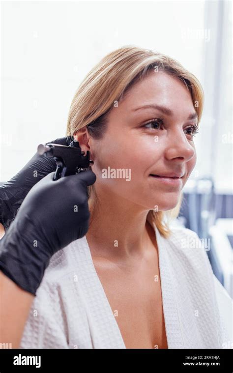 Close Up Of Face Of Young Blonde Woman Doing Ear Piercing Procedure Doctor Hands In Black