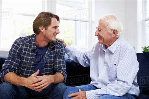 Adult Son Sitting On Sofa And Talking To Father At Home Stock Photo