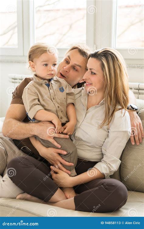 Portrait Of Happy Parents Sitting On The Sofa With Their Beautiful Baby
