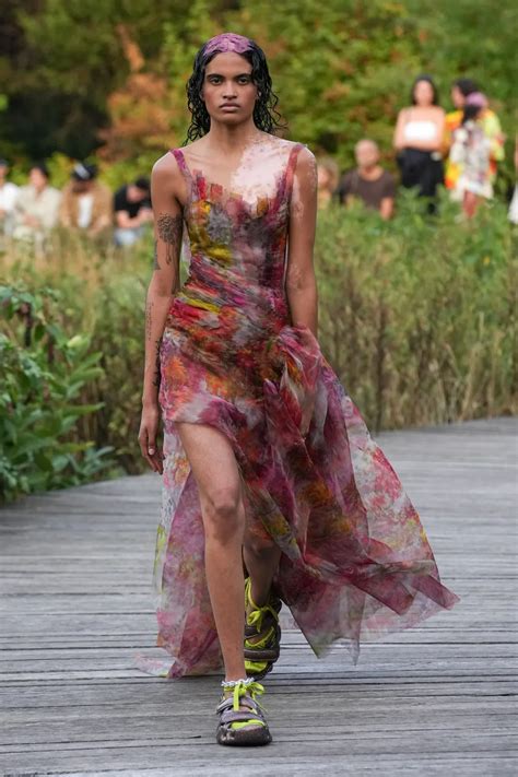A Woman Walking Down A Wooden Walkway Wearing A Dress With Flowers On