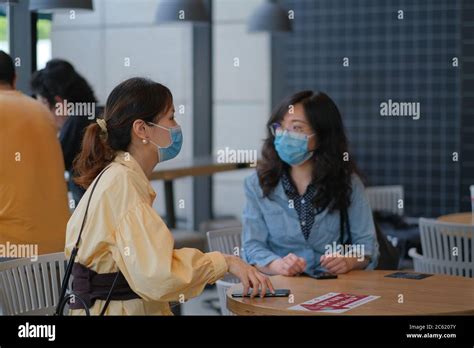 Young Women Talking In Cafe Wearing Surgical Mask To Prevent Infection
