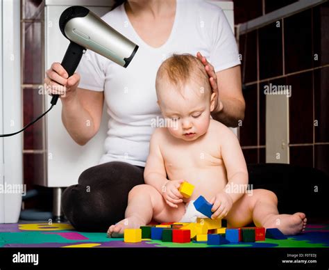Mother Drying Hair Of Her Child While Baby Is Playing With Toys Stock