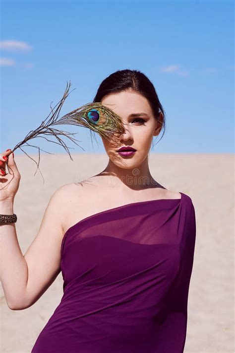 amazing beautiful brunette woman with the peacock feather in purple fabric in the desert stock