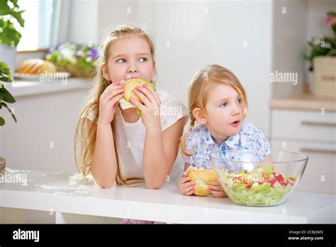 Two Children Eat Rolls With Sausage And Cheese In The Kitchen Stock