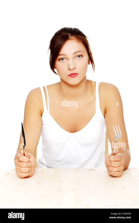 Hungry Pretty Caucasian Teenage Girl Sitting Behind The Table With Fork And Knife Isolated On