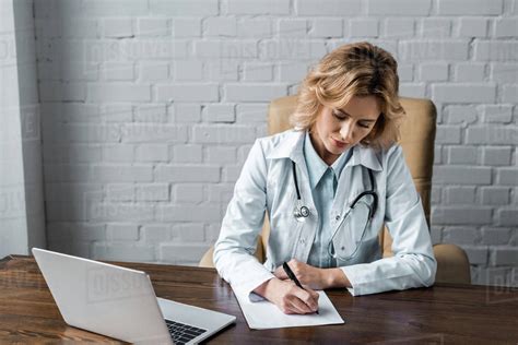 Confident Female Doctor Writing Document At Workplace In Office Stock