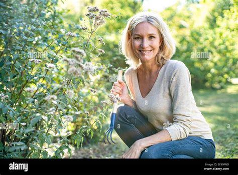 Portrait Of Smiling Mature Woman With Garden Fork Crouching In Backyard