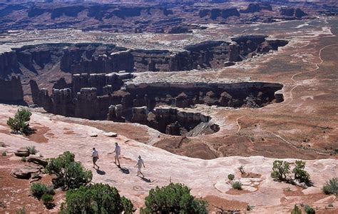 Two People Are Walking Along The Edge Of A Canyon