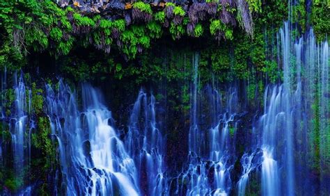 The Waterfall Is Surrounded By Lush Vegetation And Water Cascading From