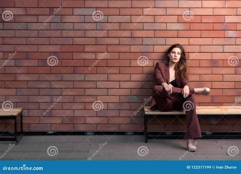 Beautiful Woman Sitting On A Bench On A Brick Wall Background Stock