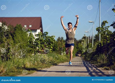 A Young Male Runner Runs With His Arms Raised In The Park Stock Photo