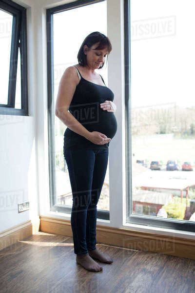 Mature Pregnant Woman Looking Out Of Window At Home Stock Photo