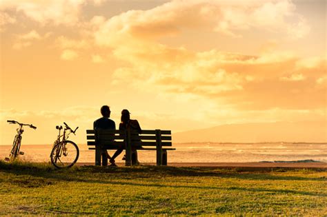 Couple Sitting On Park Bench Watching The Sunset Stock Photo Download