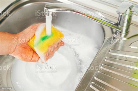 Hand Holding A Yellow Scouring Pad With A Squirt Of Green Soap On Top