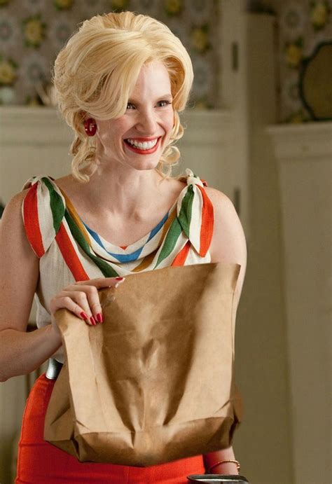 A Woman Holding A Brown Paper Bag In Her Right Hand And Smiling At The Camera