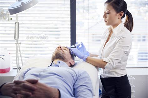 Female Beautician Giving Mature Male Patient Botox Injection In