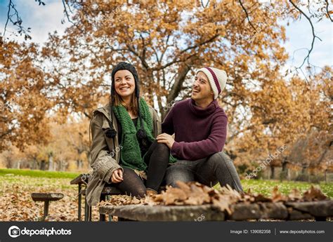 Lovely Young Couple Talking Sit In A Bench In The Park In Autum