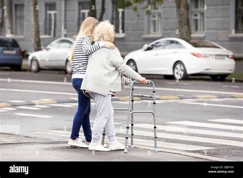Young Woman Helping Her Elderly Grandmother With Walking Frame To Cross