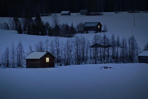 Light Glows In The Window Of A Log Cabin In A Snowy Valley At Du