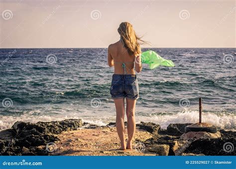 Woman Takes Off Her Clothes In The Wind While Standing On The Beach Against The Backdrop Of A